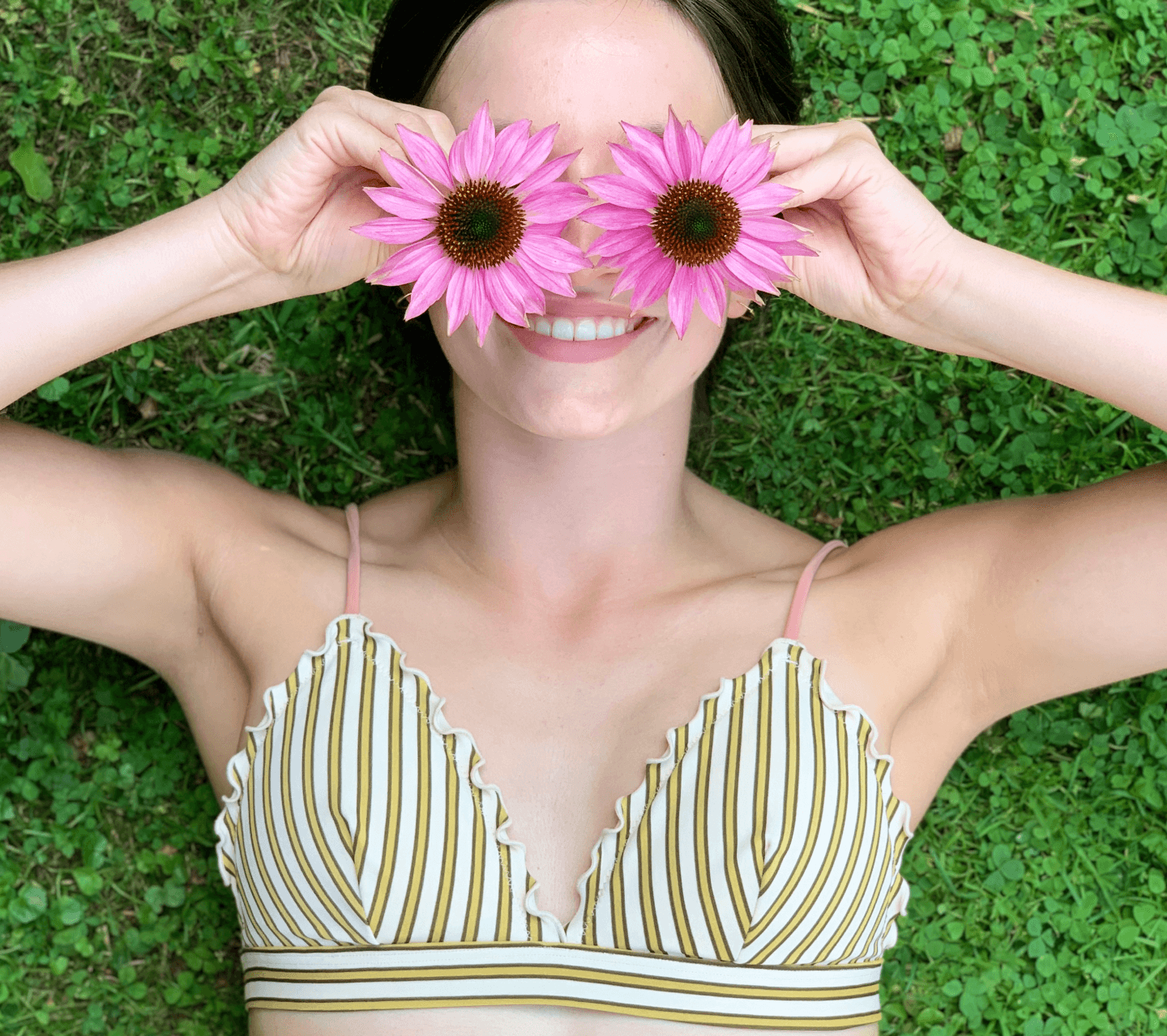 Lachende vrouw in een bikinitop die twee roze bloemen voor haar ogen houdt